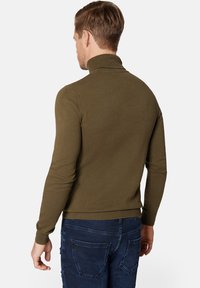 Oliwkowy sweter z golfem o dopasowanym kroju, z ribbowanymi mankietami i dołem. Nosi się go z ciemnoniebieskimi dżinsami, które mają detale na tylnej kieszeni.