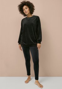 Conjunto de loungewear de felpa negra que incluye una camiseta de manga larga de corte holgado y leggings ajustados, ambos con una textura suave y un diseño minimalista.
