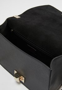 Borsa a tracolla in pelle nera con una finitura testurizzata, dotata di una chiusura in tono oro e un interno liscio. Include una tasca con zip.