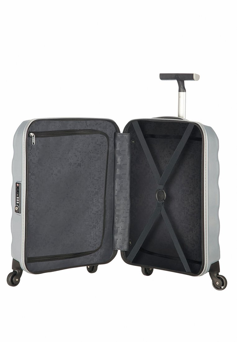 Maleta rígida gris con cuatro ruedas, mango extensible, abierta para mostrar dos compartimentos: uno con malla con cremallera y el otro con correas elásticas cruzadas.