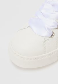 Witte leren sneaker met een gestructureerde afwerking, voorzien van witte satijnen veters en ronde oogjes. Het teengebied is rond met een platte zool.