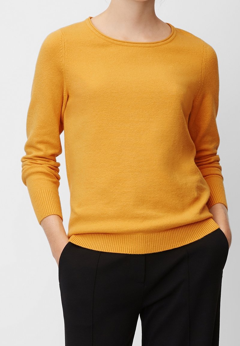 Senfgelbes Sweatshirt mit rundem Ausschnitt, gerippten Bündchen und Saum, aus weichem Material gefertigt, mit taillierter Passform. Kombiniert mit schwarzen Hosen.