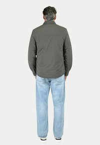 Giacca grigia scura con colletto classico, maniche lunghe e schiena dritta, abbinata a jeans azzurri svasati e sneakers nere.