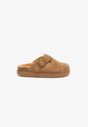 Brune suede slip-on klip med en blød pelsfor, justerbar rem og en lys brun gummisål. Glat tekstur med en rund tå.