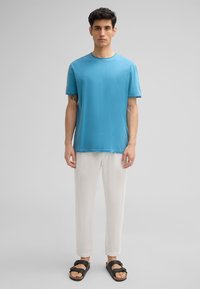 T-shirt turquoise à manches courtes en tissu doux, associé à un pantalon beige clair et des sandales noires avec des sangles réglables.