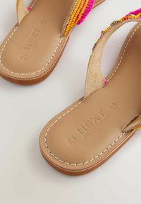 Besetzte flache Sandalen mit einem braunen Lederfußbett, die bunte rosa und gelbe Akzente an den Riemen und gestickte Details aufweisen.