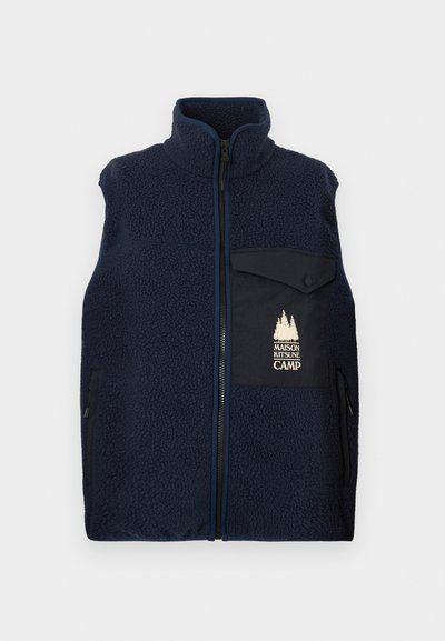 Tumši zils vilnas veste ar augsto apkakli, priekšējo rāvējslēdzēju un kreisajā krūtī kabatu ar gaišas krāsas logotipu. Tekstūrēta auduma un sānu kabatas.