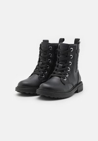 Botines negros hasta el tobillo, hechos de cuero, con punteras redondas, ojales de metal y cordones. Presentan un cierre lateral con cremallera y una suela texturizada para mayor agarre.