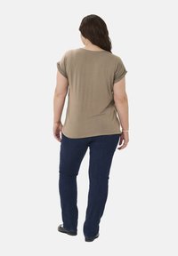 Oliven grøn kortærmet top med rund halsudskæring, løs pasform og blød tekstur, parret med mørkeblå jeans og sorte sko.