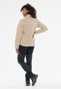 Beige fleecejacka med hög krage, texturerad yta och svarta byxor. Svarta vandringsskor med slitstarka sulor fullända ensemblen.