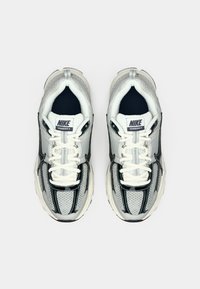 Nike Vomero 5 Sneaker mit einem Obermaterial aus Mesh in Weiß und Marineblau, reflektierenden Akzenten, dicker Zwischensohle und traditionellem Schnürsystem.