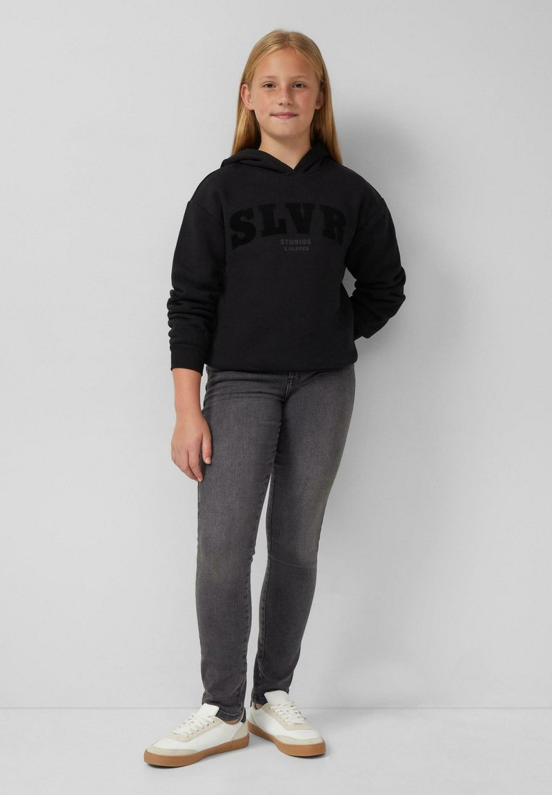 Felpa nera con logo "SLVR", jeans slim-fit grigi e sneakers bianche con dettagli marroni. Tessuto morbido, design casual. Sfondo neutro.