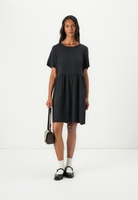 Dunkelblaues Kurzarmkleid mit gerafftem Bund, glatter Textur und knielangem Schnitt, kombiniert mit schwarzen Schuhen und einer Umhängetasche.