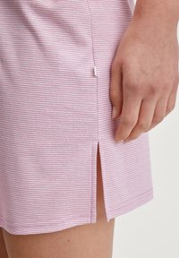 Gonna in tessuto a righe rosa con dettaglio di spacco laterale, morbida al tatto e con orlo dritto. Mano appoggiata sul tessuto, evidenziando la trama.