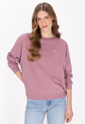Lichtroze sweatshirt met een ontspannen pasvorm, ronde hals en lange mouwen. Bevat subtiele branding op de borst. Gecombineerd met lichtblauwe jeans.