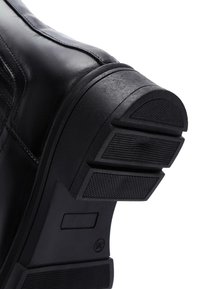 Zwarte leren schoenzool met een getextureerde rubberen grip, voorzien van een meerlaag ontwerp en een lichte hakverhoging.