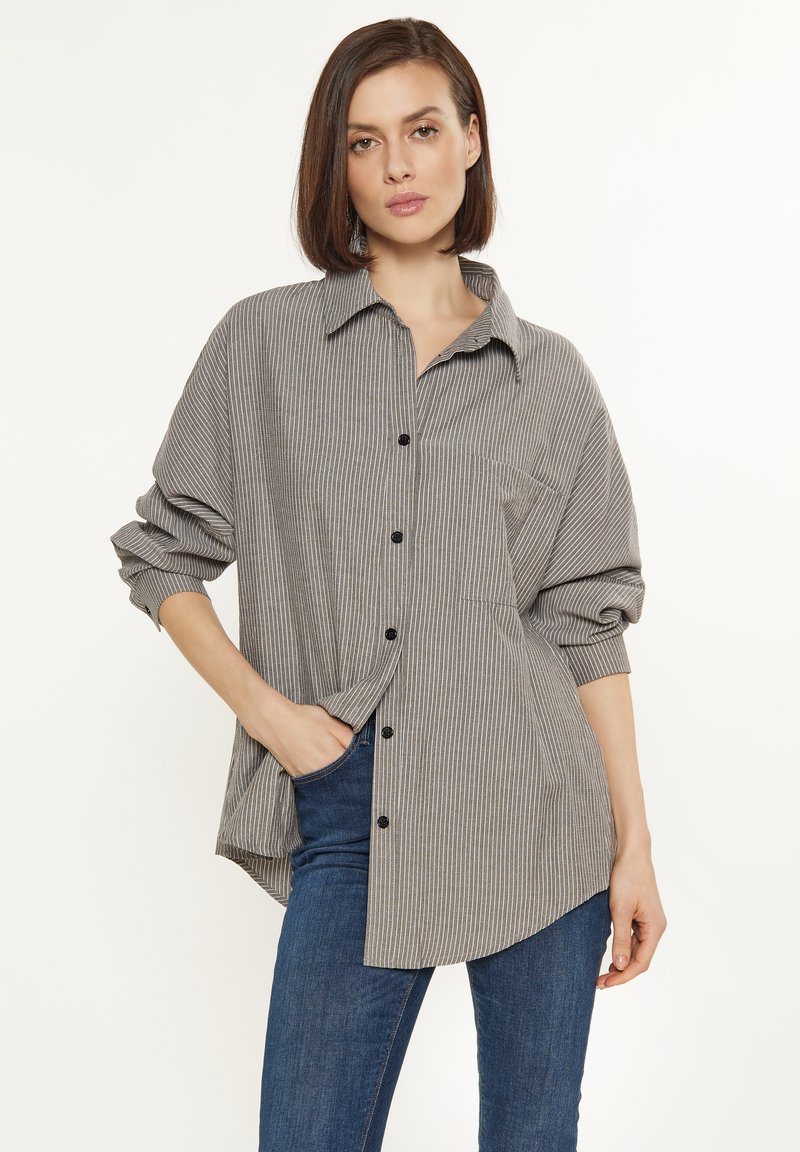 Camicia a righe grigia e bianca con colletto, taschino sul petto e maniche lunghe con risvolti. Presenta bottoni neri visibili.