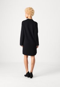 Čierne šaty s dlhými rukávmi, okrúhlym výstrihom a perlami na manžetách. Hladká textúra, dĺžka po kolená a strih na mieru.