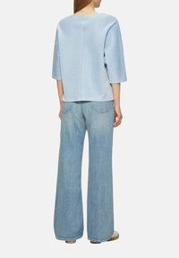 Lichtblauw gebreid topje met een textuur gestreept patroon, voorzien van driekwart mouwen en een ontspannen pasvorm, gedragen met hoge taille wijd uitlopende jeans.