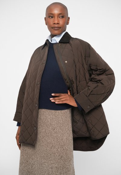 Καφέ καπιτονέ jacket με κουμπιά σnap, μεγάλο γιακά και χαλαρή εφαρμογή, επάνω από έναν ναυτικό πουλόβερ και μια μπεζ υφασμένη φούστα.