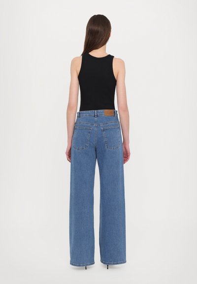 Wide-leg blue denim jeans with a high waist, featuring two back pockets and a brown label on the waistband, paired with a black tank top.