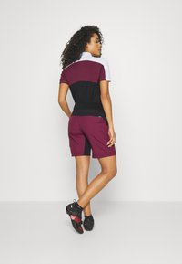 Maroon, juodai ir baltai trumpomis rankovėmis sportinis marškinėliai, derinami su maroon šortais. Audinys atrodo lygus, su kontrastingais akcentais. Reguliuojamas juosmens diržas.