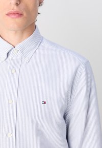 Camisa de botones a rayas azul y blanca con cuello tipo spread, pequeño parche con logo en el pecho y dobladillo redondeado. Tejido de algodón, diseño texturizado.