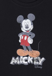 Camiseta negra con un gráfico desgastado de Mickey Mouse en gris y rojo, con la palabra "MICKEY" en letras blancas, negritas y estilizadas.
