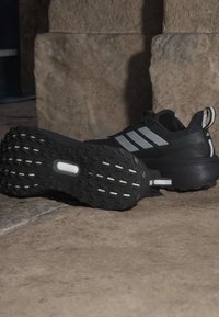 Sort atletiksko med textureret gummisål, der har tre grå striber på siden og en pull-tab ved hælen. Solid design.