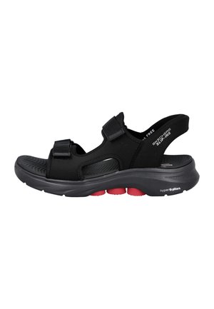 Sandalia negra Skechers tipo slip-on con correas ajustables, suela acolchada y cámaras rojas absorbentes de impactos en la suela exterior.