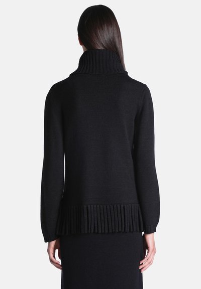 Femme debout de dos portant un pull à col roulé côtelé noir avec manches longues et détail de bord côte.