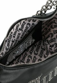 Bolso de cuero negro con cremallera plateada y correa de cadena. El interior cuenta con un forro estampado en blanco y negro con el texto "Juicy".