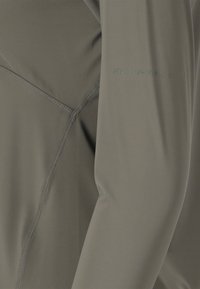 Close-up of khaki fabric with visible stitching and faint "ENDURANCE" text on smooth, stretchy material, likely athletic apparel sleeve.