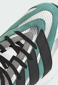 Sport-Schuhe mit einem Obermaterial aus Mesh in Weiß, tealfarbenen Wildlederelementen, schwarzen synthetischen Streifen, grauen Wildlederelementen und schwarzen Schnürsenkeln.