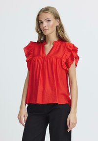 Blusa rossa a maniche corte con dettagli arricciati, scollo a V e vestibilità ampia, realizzata in tessuto leggero con una superficie leggermente strutturata.
