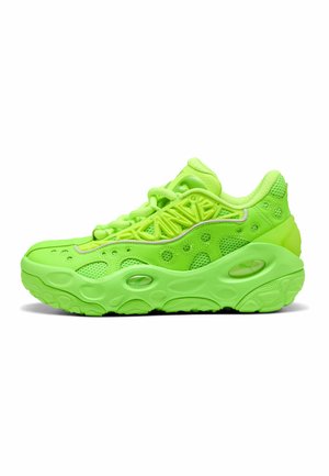 Zapatilla deportiva de color verde brillante con suela texturizada, paneles de malla y patrones geométricos a lo largo de los lados y la parte superior, mostrada en perfil lateral.