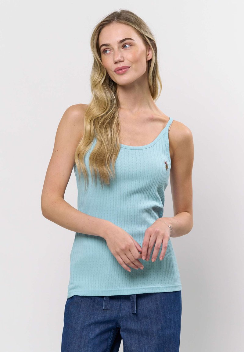 Šviesiai mėlynas, briaunuotas marškinėlių liemenė su plonomis petnešėlėmis, pasižyminti subtilia tekstūra ir mažu siuvinėtu detaliu, derinama su aukšto liemens džinsiniais kelnėmis.