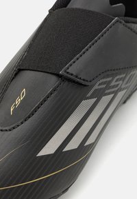 Melna futbola kurpe ar teksturētu virsmu, ar sudraba svītrām un zelta "F50" zīmolu. Iekļauta elastīga siksna drošai piestiprināšanai.