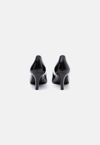 Escarpins en cuir verni noir avec un design élégant, bout pointu et talon aiguille fin. Texture lisse et couture minimaliste visibles.