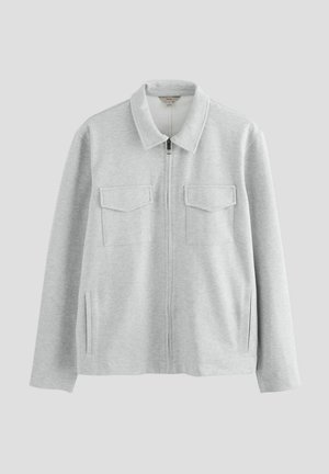 Chaqueta gris con cremallera, hecha de tela suave, con cuello tipo solapa, dos bolsillos en el pecho y aberturas laterales para mayor comodidad.