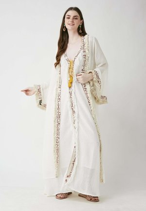 White kimono-style dress with flared sleeves, featuring red wavy patterns and fringe accents. Tied with a yellow cord. Smooth, lightweight fabric.