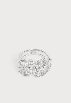 Bague double en argent avec plusieurs pierres précieuses transparentes de formes différentes regroupées sur le dessus sur un fond blanc uni.