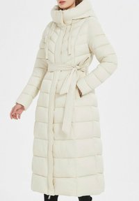 Manteau rembourré long de couleur crème avec une capuche. Il possède une ceinture à la taille, des coutures verticales et une fermeture éclair pleine longueur.