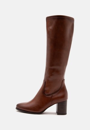 Botte haute en cuir marron à bout arrondi et talon haut épais, présentée de profil sur un fond clair uni.