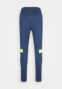 Pantalones deportivos azul marino con cintura elástica, que presentan dos franjas amarillas neón en la parte inferior de las piernas y bajos con cremallera.