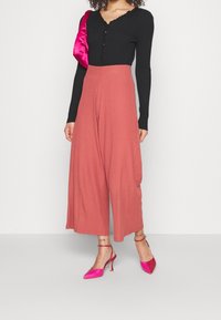 Zwart geribbelde top met lange mouwen en een scalloped halslijn, gecombineerd met lichte roze wijde broek en felroze hoge hakken.