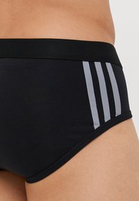 Musta kangas alushousut, joissa on muotoon leikattu malli, pehmeä rakenne ja kolme pystysuoraa harmaata viivaa sivuilla. Joustava vyötärö, joka tarjoaa mukavuutta.