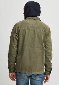 Khaki jakke med lige pasform, knapmanchetter og et rygstykke detalje. Båret over en marineblå hoodie lavet af en bomuldsblandingsstof.