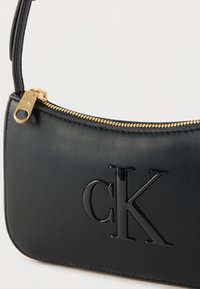 Μαύρη δερμάτινη γυναικεία τσάντα με ανάγλυφο λογότυπο CK, χρυστό φερμουάρ και αντίστοιχο χρυσό τράβηγμα φερμουάρ, με λεπτό λουρί ώμου.