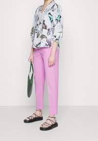 Blusa azzurro chiaro con stampa di farfalle, maniche tre quarti; pantaloni rosa su misura; sandali neri con cinturini; borsa verde.